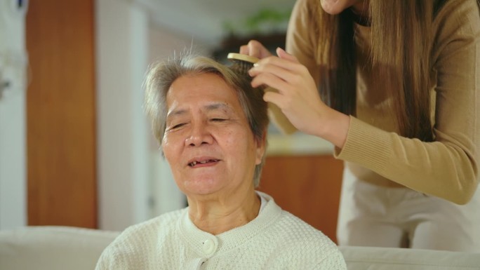 亚洲妇女在家中客厅为老年妇女梳头。