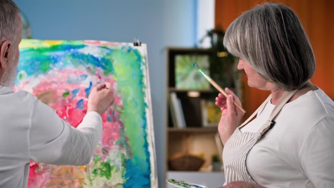 退休爱好，开朗的男女退休老人学习现代艺术，在家里用颜料和画笔创作图画