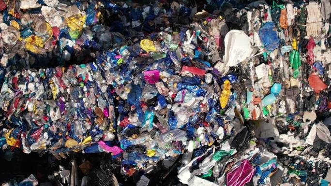 在露天的废物回收厂，多个立方体压缩的彩色塑料垃圾