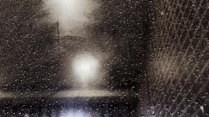 夜晚，雨点落在窗玻璃上，玻璃反射在室内的背景中。