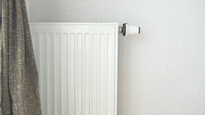 灰白色墙壁上的白色暖气片。公寓供暖安装系统;