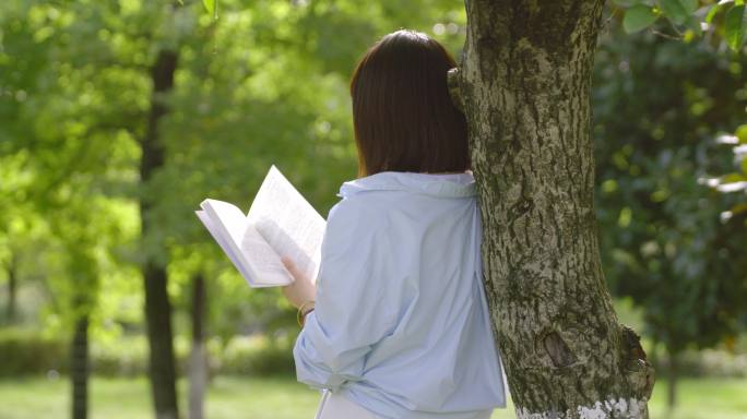 女人踩草地树下看书顶着书奔跑