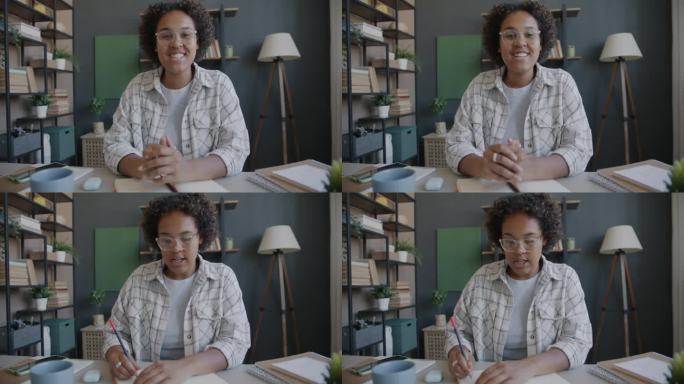 非裔美国女孩在网上学习，在笔记本上写信息，看着相机，在家里说话的肖像
