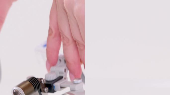 女性的手从桌子上拿双筒望远镜牙科器具用于治疗牙龈牙齿修复体填充管道放大图像供外科医生在口腔外科手术中
