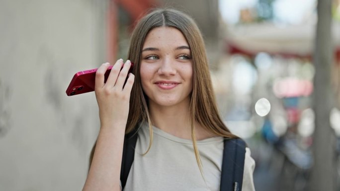 年轻漂亮的女学生背着背包在街上用智能手机听语音信息