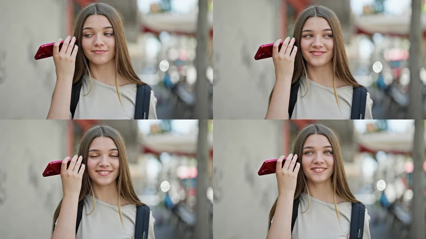 年轻漂亮的女学生背着背包在街上用智能手机听语音信息
