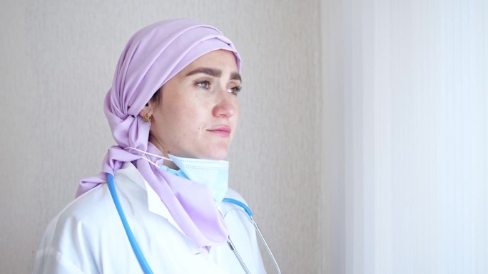 疲惫的穆斯林医生戴着头巾望着窗外，摘下口罩