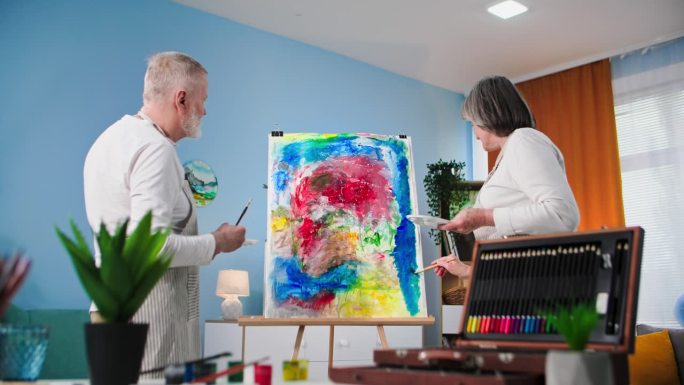 现代爱好，有创意的老年男女喜欢在家里用毛笔和颜料在画布上作画