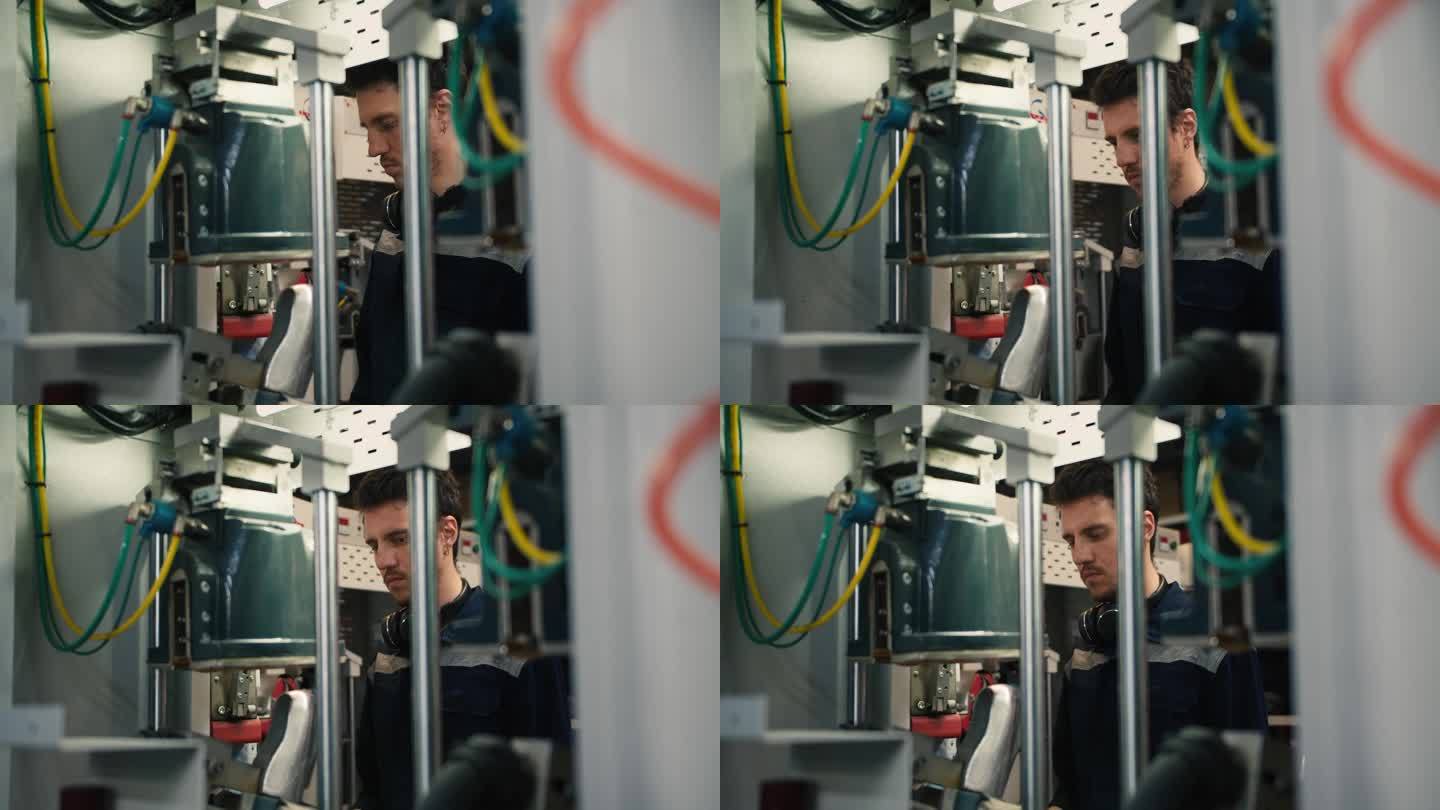 在一家工厂里，一名身穿蓝色制服、头戴黑色耳机的男子站在机器后面，确保机器正常工作