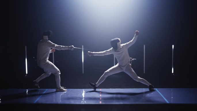 两名职业击剑手在灯光明亮的舞台上进行战斗。猛扑进攻，一击而中