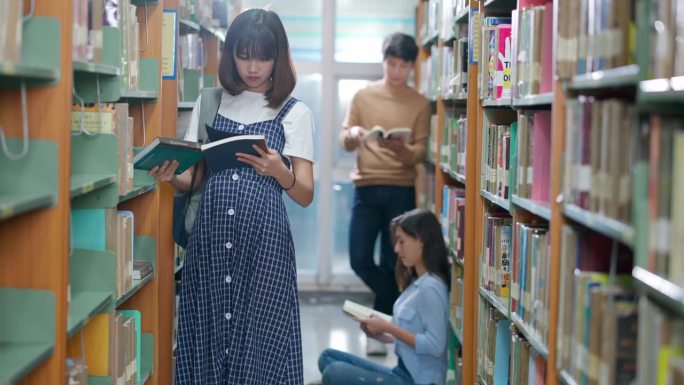 一名女大学生在大学图书馆的书架上找书