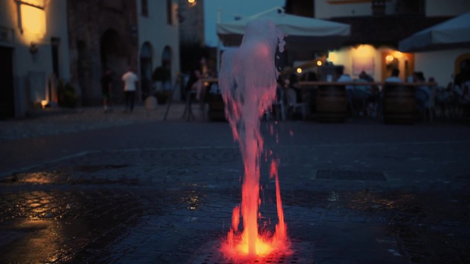 行人或地面喷泉。街上的喷泉。广场上的公共喷泉。特写镜头。水柱上升，溅落在铺路石上。炎热的夏夜。欧洲的
