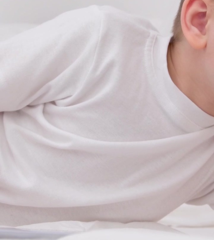 7岁的小男孩躺在床上手里拿着平板电脑在线学习有趣的电影手机游戏英语课程隔离躺在床上恢复东亚眼睛黑头发