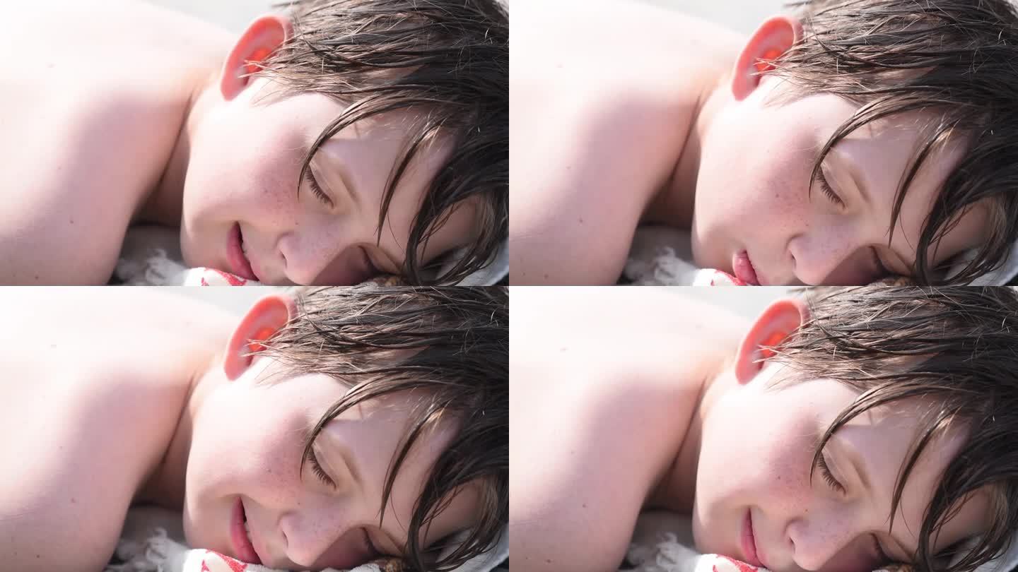 一张10岁男孩的脸，头发湿漉漉的躺在沙滩上。孩子躺着，在阳光下晒日光浴。