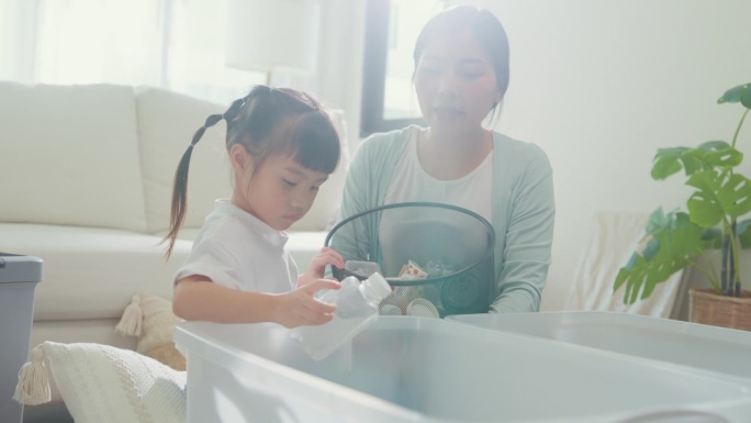 年轻的亚洲家庭的特写妈妈教孩子如何回收帮助女孩意识到环境的重要性在家里的客厅。家庭幸福时刻概念。