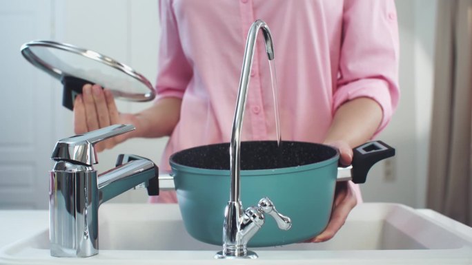 厨房里的女人用手把过滤过的水抽到一个绿松石壶里，水从一个小的过滤水龙头流出。过滤龙头在中间，中拍，4