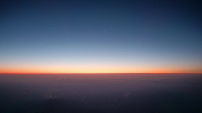 从山顶观看日出的4K延时镜头，天空中的星星仍然在天空中，云下的城市灯光，太阳升起前天空背景颜色变化。