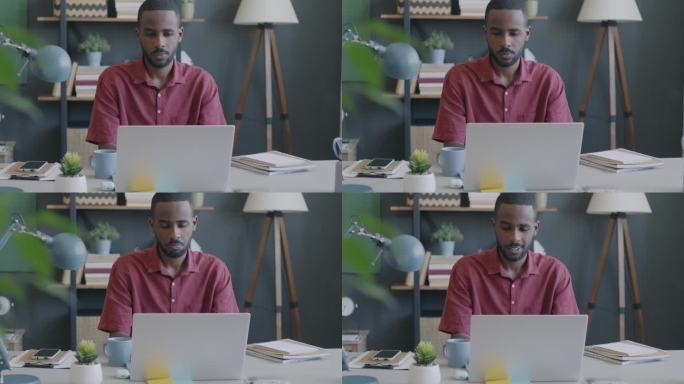 年轻的非洲裔美国学生在网上用笔记本电脑学习，在家里的办公桌前微笑