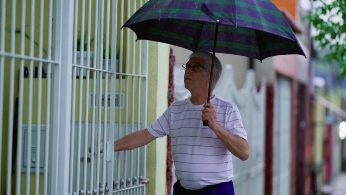 老人冒雨回家，撑开雨伞，锁好大门，走在人行道上
