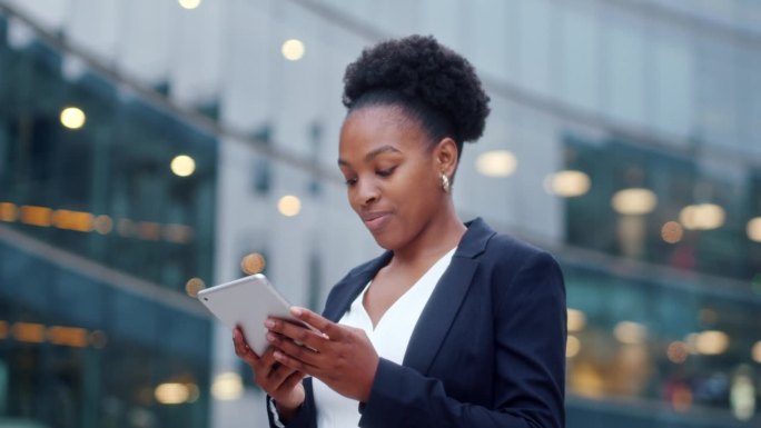 快乐的非裔美国女商人站在办公室大窗户旁边使用平板电脑。女人翻页，点击触摸屏，查看财务图表。关闭了。