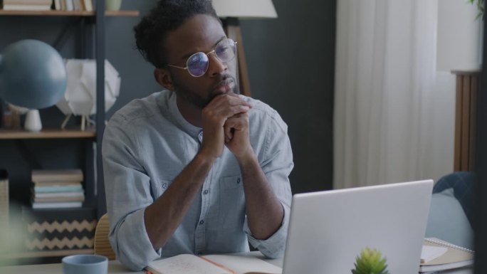 一个深思熟虑的非裔美国人坐在家里的办公桌前寻找商业创意