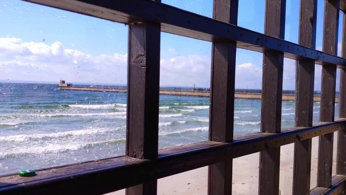 大海在一扇大木框窗后，在蓝天的映衬下起伏