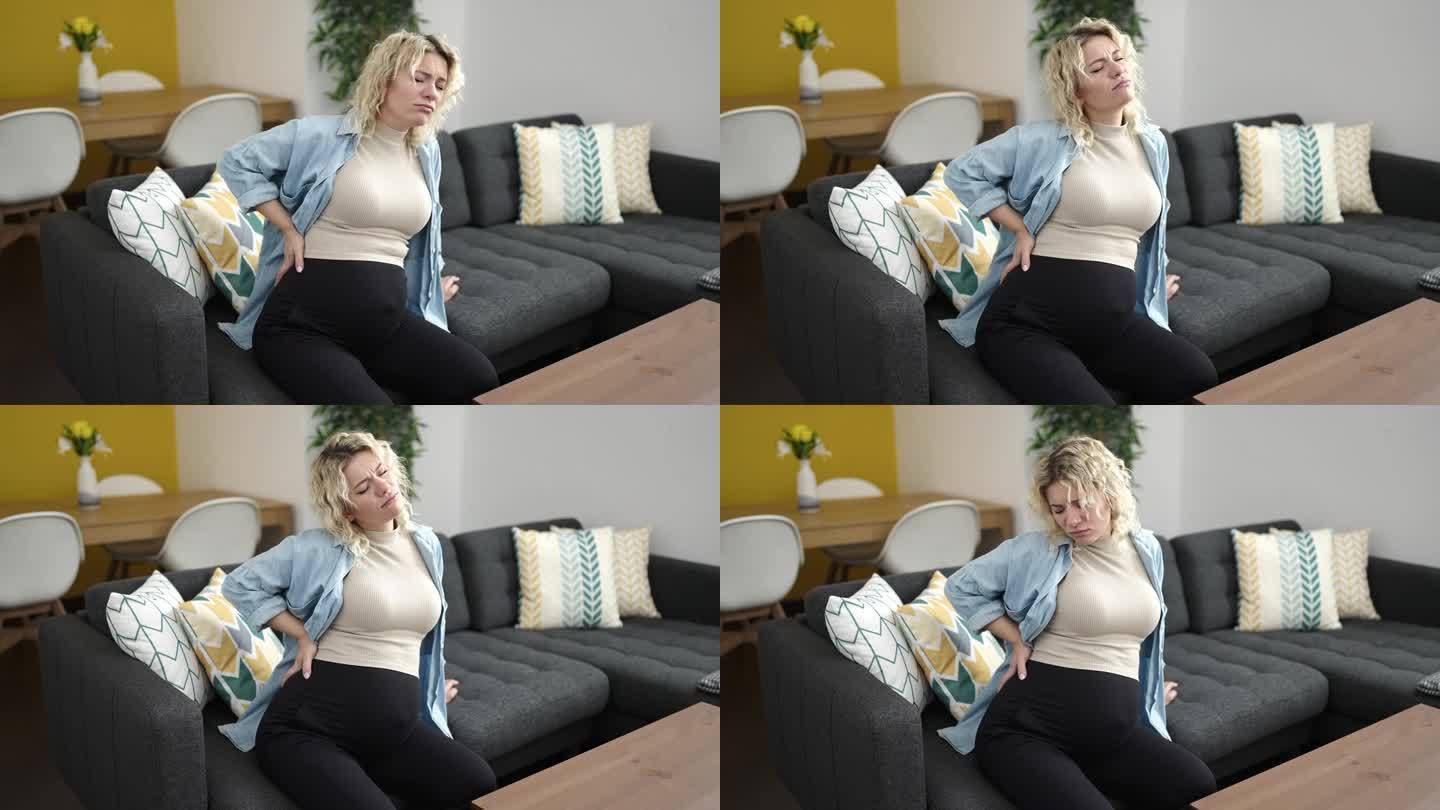 一位腰酸背痛的年轻孕妇坐在家里的沙发上