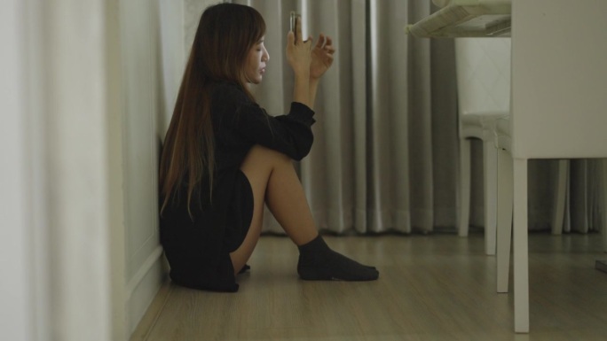 年轻的亚洲女子坐在地上，膝盖翘在地上，试图用智能手机给男友打电话，但没有人接。所以，她感到心烦意乱，