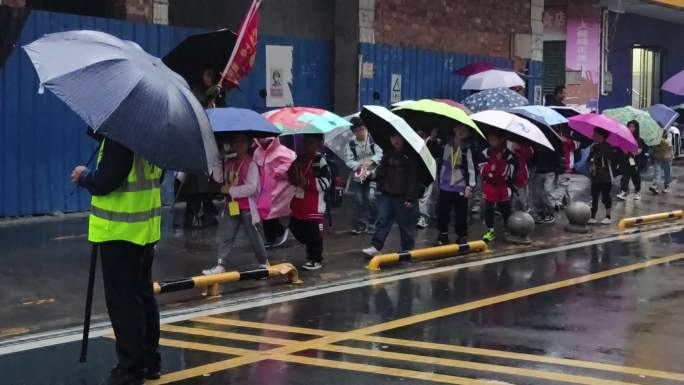 雨天放学小学生放学家长接送校门冒雨伞走路