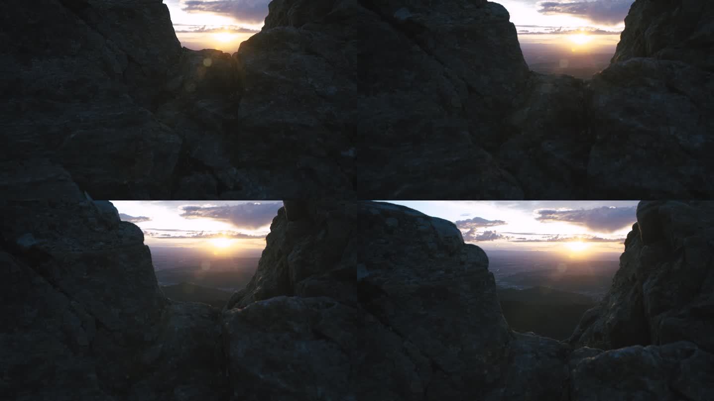 夕阳落在连绵起伏的山丘上，天空五彩缤纷，前景是岩石