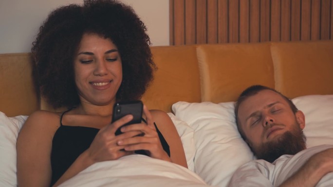 非裔美国女人和丈夫躺在床上发短信，出轨