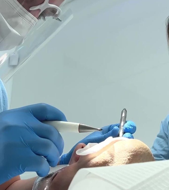 牙科专业医生治疗牙齿，以一名男子加工眼镜，特殊面具，蓝色t恤在白厅工具最新技术修复治疗手术补牙