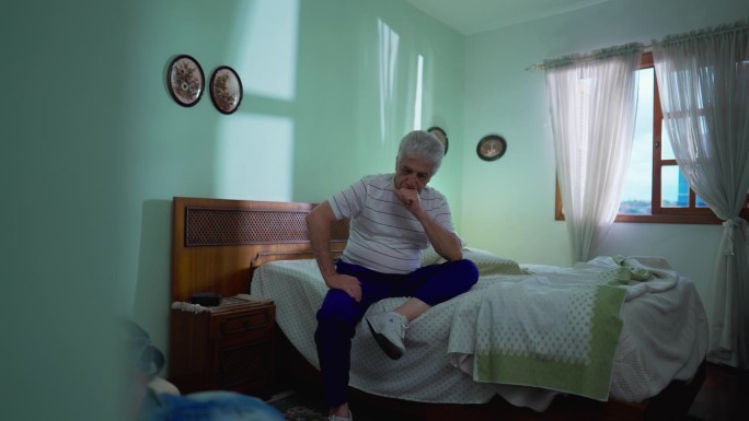 一位深思熟虑的老人坐在卧室的床边忧郁地沉思。老人的肖像描绘了老年，挣扎于困境，思考着抉择