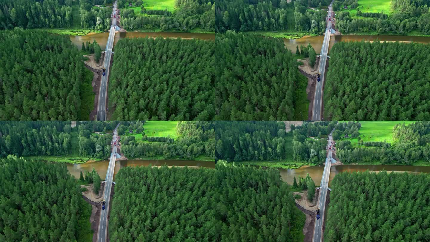 从拉脱维亚的无人机拍摄的绿色森林和棕色浑浊河流之间正在建设的道路。
