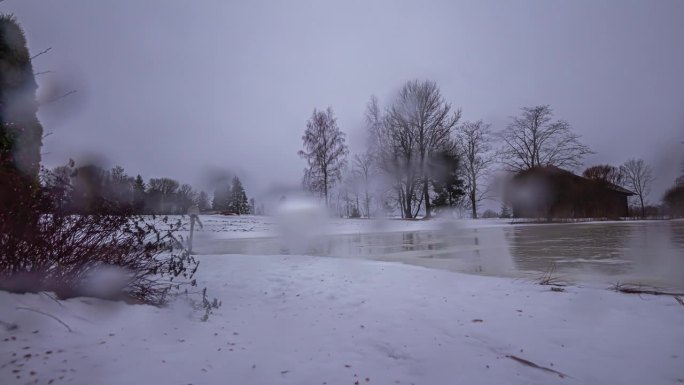 在拉脱维亚乡下，一个冰冻的湖泊和谷仓的镜头上有雨滴的延时冬季背景。
