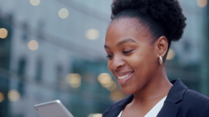 快乐的非裔美国女商人站在办公室大窗户旁边使用平板电脑。女人翻页，点击触摸屏，查看财务图表。关闭了。
