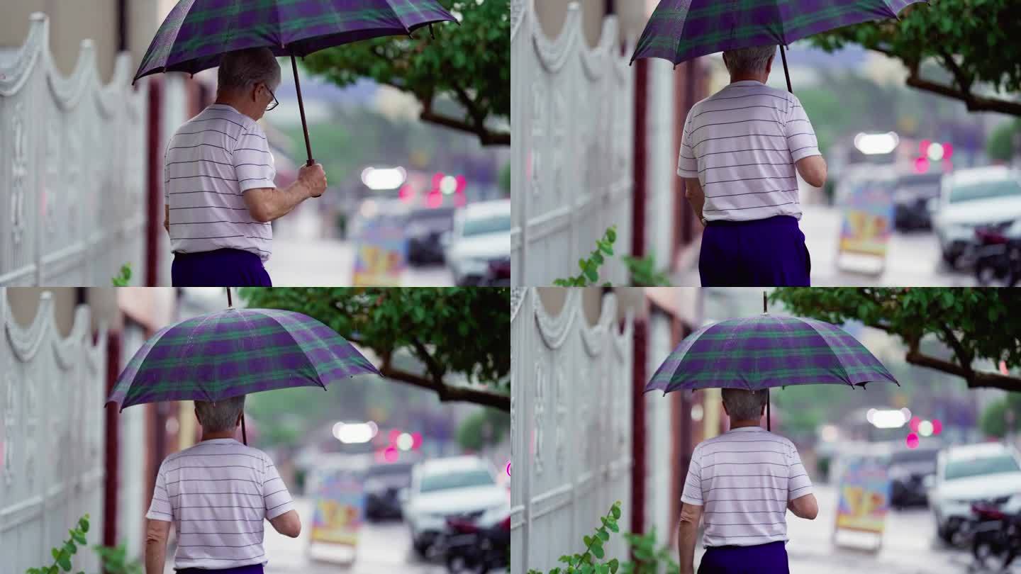 老人的背影在雨中打着伞走着。上了年纪的人在雨中漫步在人行道上