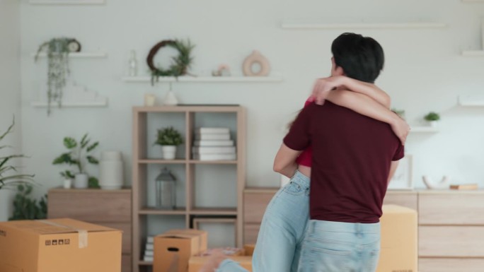 亚洲年轻的成年夫妇互相拥抱，以显示他们的爱，同时协助安排在新房子里的东西。