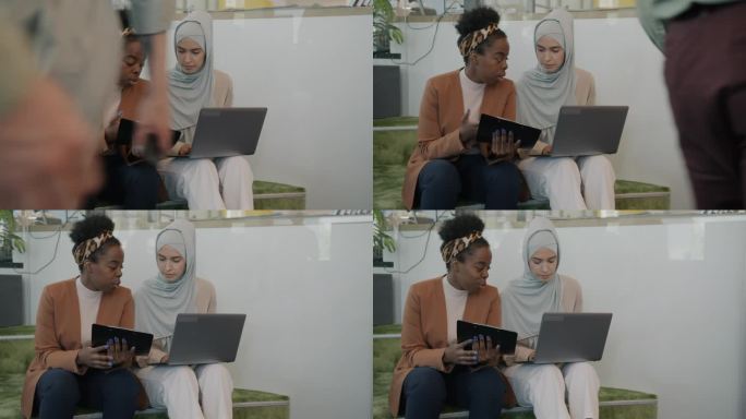 年轻的女同事在现代的共同工作场所用笔记本电脑交谈和工作