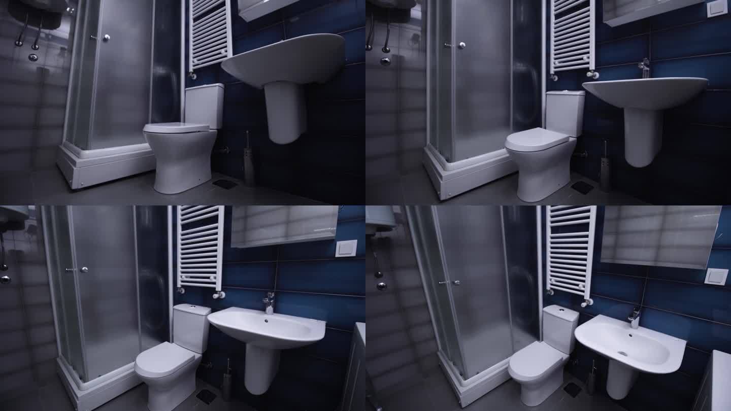现代公寓里的浴室。崭新干净的马桶，贴着蓝灰瓷砖。垂直摄像机移动。