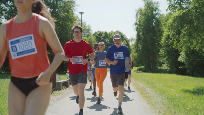 慢动作多莉拍摄:肖像的不同群体的人参加马拉松和通过公园小径跑。慢跑者在友好赛跑中随意争夺第一名