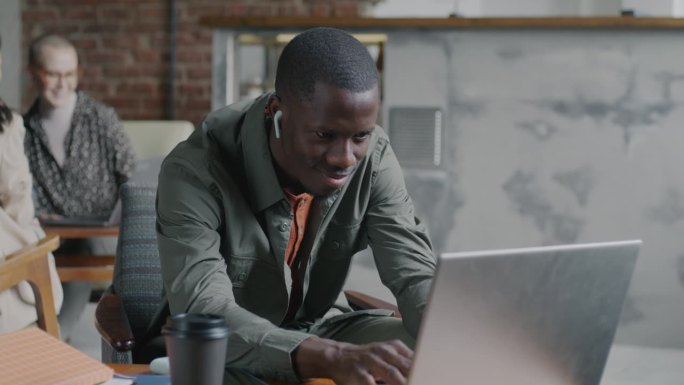 非裔美国自由职业者在咖啡馆用笔记本电脑打字，戴着耳机听音乐