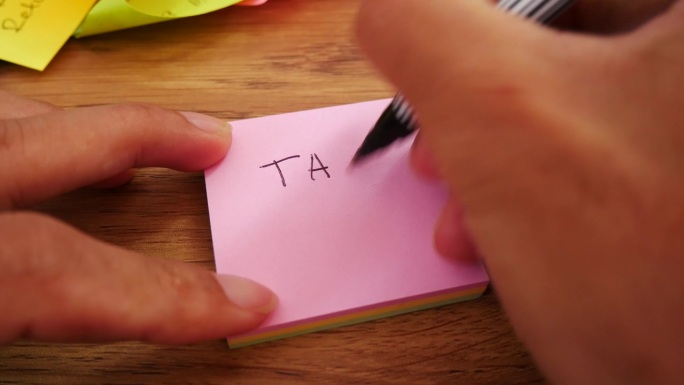 男子用黑笔和柔焦场景在黄色纸上写TAX 2023票据。
