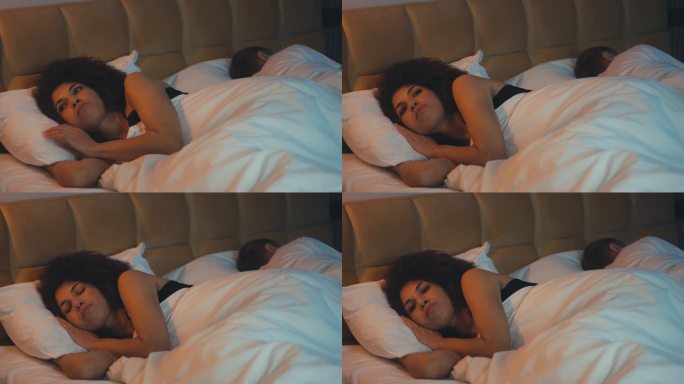 沮丧的年轻女子躺在床上失眠的丈夫旁边，不幸的婚姻