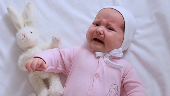 一个刚出生的小女孩在家里的白色棉质床上哭泣的特写，一个小孩的哭泣和眼泪