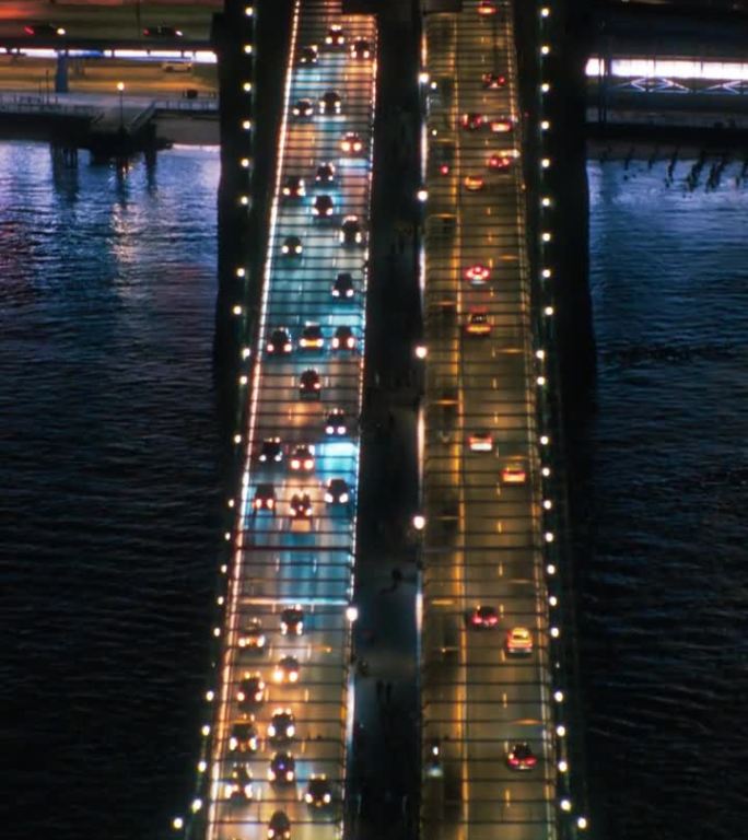 垂直屏幕:空中俯视夜景与布鲁克林大桥与汽车在道路上的两个方向移动。直升机鸟瞰一个受欢迎的美国旅游和商