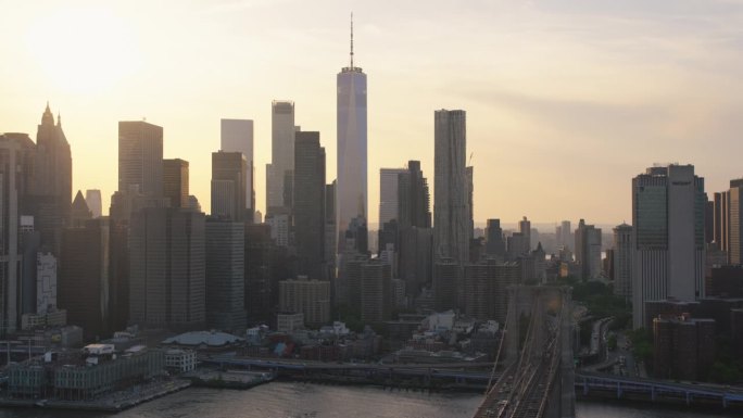 空中直升机电影场景在布鲁克林大桥与曼哈顿摩天大楼的城市景观。美丽的晚霞闪耀着温暖的晚霞。聚焦世贸中心