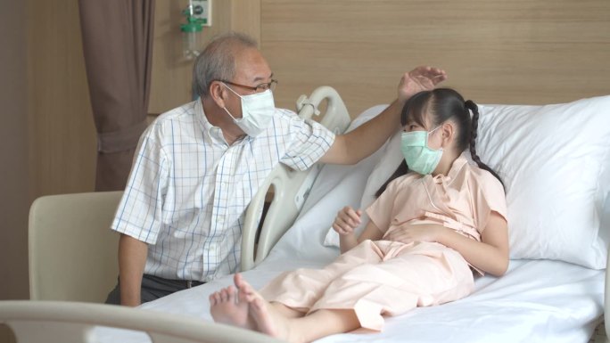 戴着口罩照顾生病的小女孩的亚洲老人。