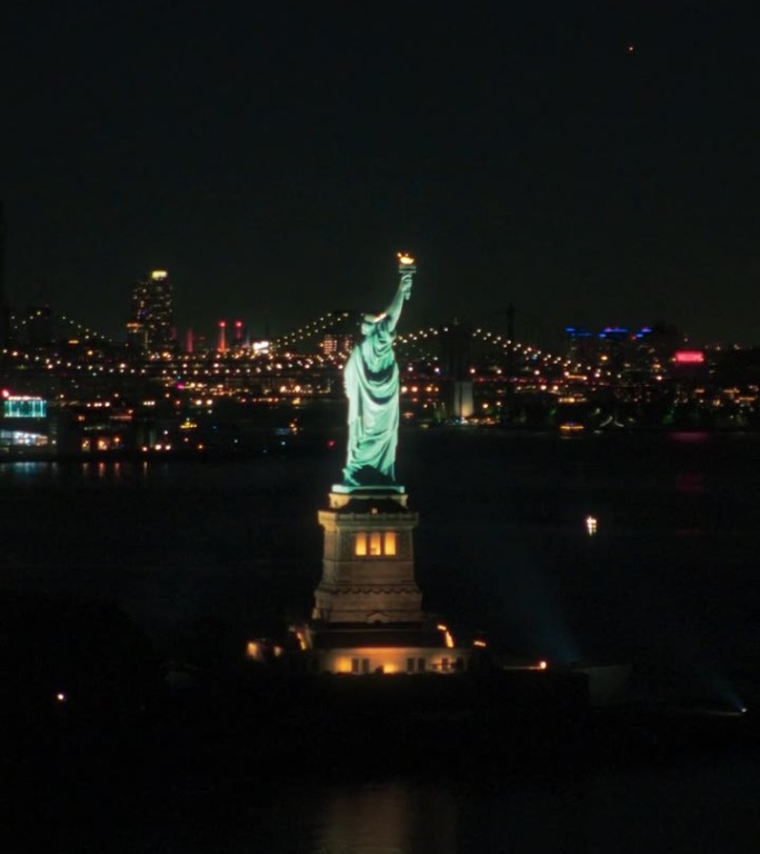 垂直屏幕:自由女神像的鸟瞰图。曼哈顿和布鲁克林办公大楼在夜晚灯火通明的标志性旅游目的地。纽约的夜生活