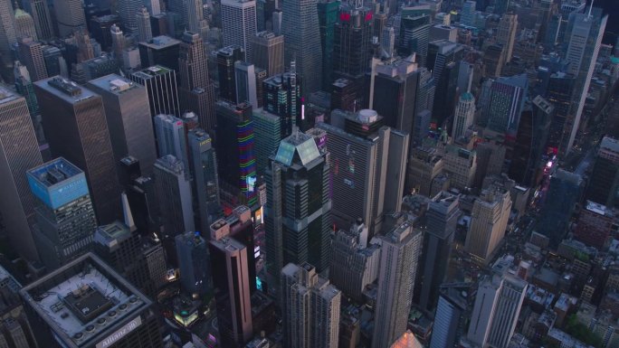 高角度空中直升机镜头在曼哈顿中城摩天大楼的城市景观与灯光从窗户，照明，广告牌。美丽的夜晚，温暖的夕阳